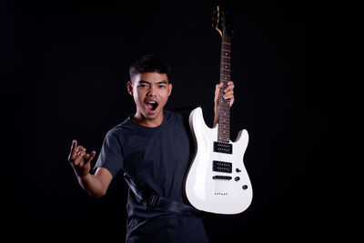 Young man playing guitar against black background