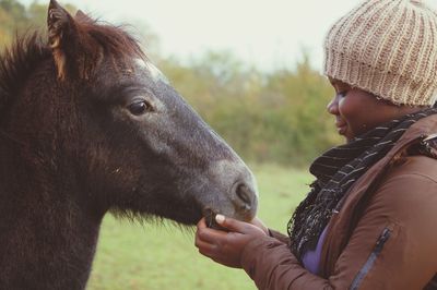 Smiling woman touching horse on field against sky