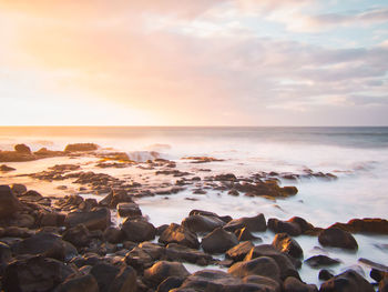 Rocks on beach against sky during sunset