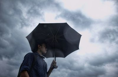 Low angle view of man holding umbrella against sky during rainy season