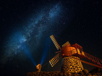 Low angle view of couple standing by windmill against star field at night