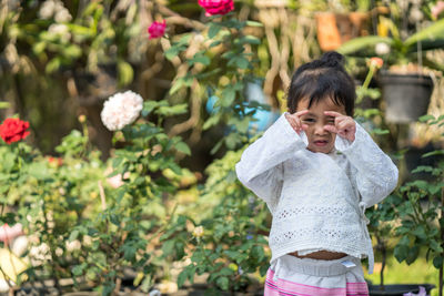 Portrait of girl gesturing while standing by flowering plants at park