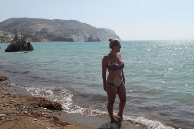 Woman in bikini with ostomy bag on her stomach while standing at seashore