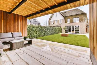 Terrace of residential building with comfortable couch under roof on wooden shed with grassy lawn growing in suburb area