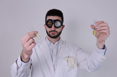 Portrait of young man holding eyeglasses against white background