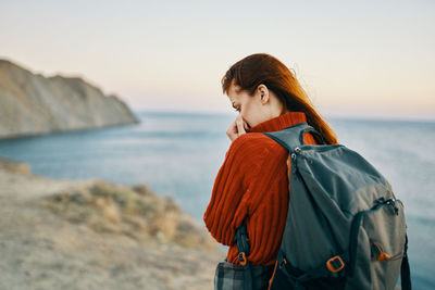 Young woman standing at beach against sky