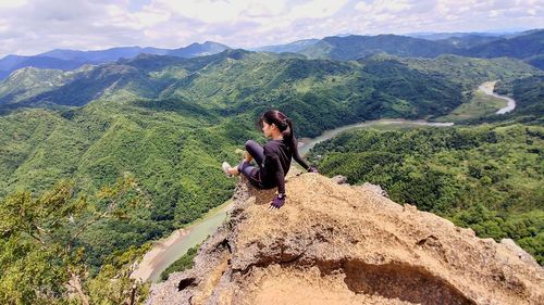 Young woman sitting on mountain against sky