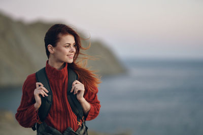 Young woman looking away while standing against sea