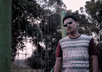 Young man wearing sunglasses standing against trees