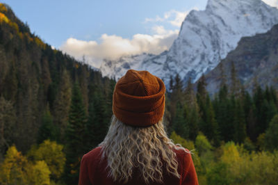 Blonde woman standing with her back to the camera and watching magical clouds in a mountainous area