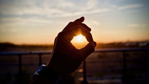 Cropped hand showing ok sign against sky during sunset