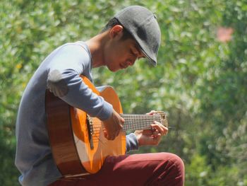 Side view of young man playing acoustic guitar against plants