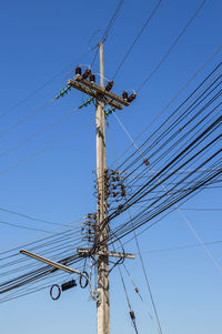 Low angle view of electricity pylon against clear blue sky