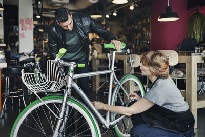 Female mechanic analyzing bicycle while talking to customer in repair shop