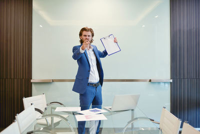 Full length of man holding camera while standing indoors