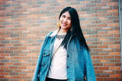 Portrait of smiling young woman standing against brick wall