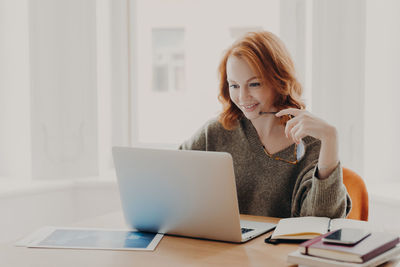 Portrait of smiling woman using phone while sitting on table