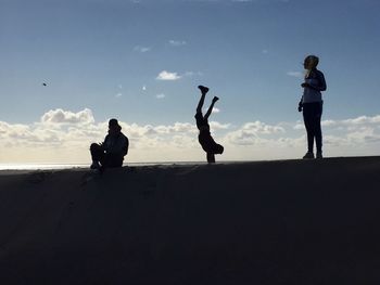 Low angle view of friends enjoying at beach against sky