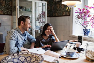 Happy father looking at smiling son using laptop for homework at home