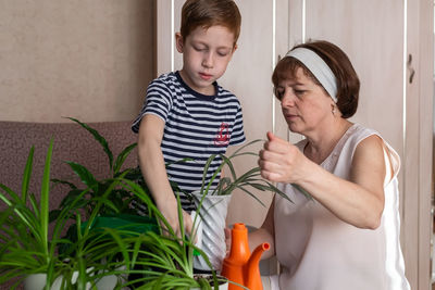 Grandmother and her little grandson red-haired boy 6-7 years old watering flowers together, fun