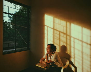 Young woman sitting on chair against wall