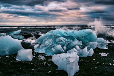 Snow covered rocks in sea against sky