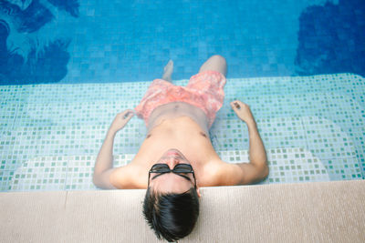 High angle view of shirtless man relaxing in swimming pool