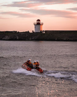 Lighthouse on sea against sky during sunset