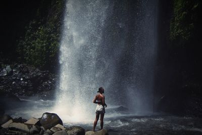 Rear view of woman standing against waterfall