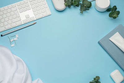 Blue desktop with pink gerbera flowers, keyboard and mouse. notepad and cosmetics.