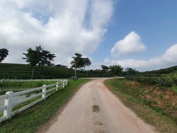 Dirt road amidst field against sky