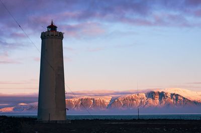 Lighthouse by building against sky during sunset