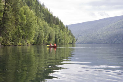 Rear view of men sitting in boat on lake against sky