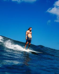 Full length of shirtless man in sea against blue sky