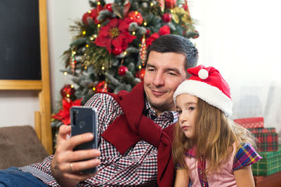 Portrait of happy young man using mobile phone at christmas tree