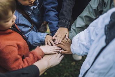 Playful multiracial preschool students stacking hands with teacher in park
