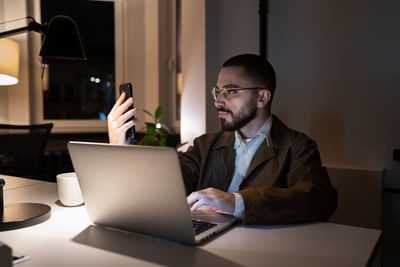 Busy front end developer or qa engineer testing app on smartphone work overtime in coworking space