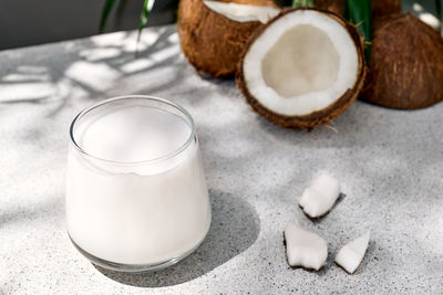 Coconut milk in glass and half of coconut on palm leaf background. vegetable milk,lactose free drink