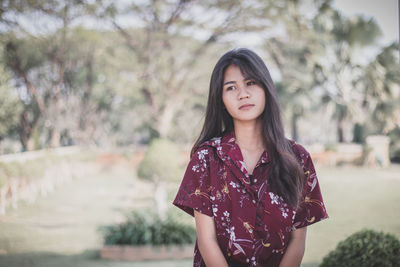 Portrait of a beautiful young woman standing against trees