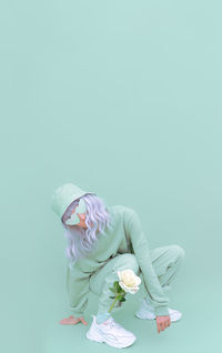 Full length of woman crouching with flower over colored background