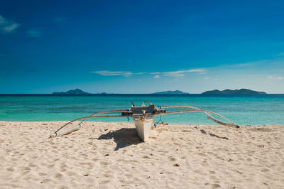 Outrigger boat on shore at beach during sunny day
