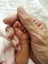 Close-up of parent and baby holding hands on bed