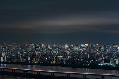 Illuminated cityscape by river against sky at night