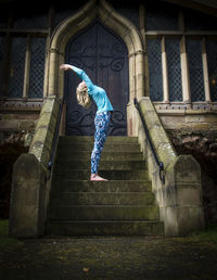 Side view of young woman practicing yoga on staircase against church