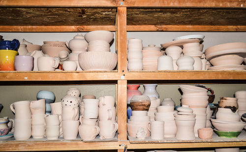 Bright pottery. many white, not painted clay pottery standing on wooden shelves
