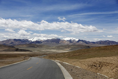 A flat and uninhabited asphalt road leads to the distant snowy mountains