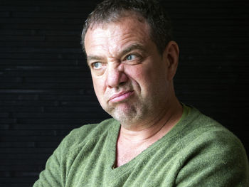 Close-up of mature man looking away while making face at home