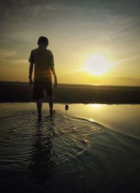 Rear view of silhouette man standing by sea against sky during sunset