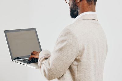 Midsection of man using laptop while standing against white background