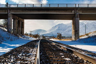 Railroad tracks by snowcapped mountain against sky